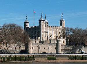 A stone castle with four towers rises above a gatehouse and other walls.