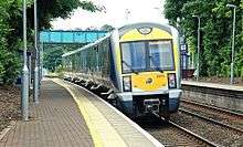 A modern train approaches the outdoor platform of a small station.