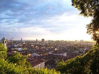 The sun, low on the horizon, bathes a small city in light; the light casts deep shadows on tiled roofs, church towers, gardens and walls.