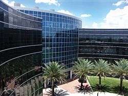 A modern architectural style building is seen clad in metal and glass against the backdrop of trees and a blue sky.