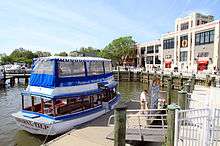 Modern color photo of a boat on a sunny day docked to a wharf with a large building behind it