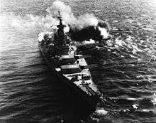 A large ship resting on the ocean, with smoke visible from the back of the vessel.