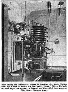 Black and white picture of a cabin. In a corner, intricate apparatus is mounted on a wall above a desk