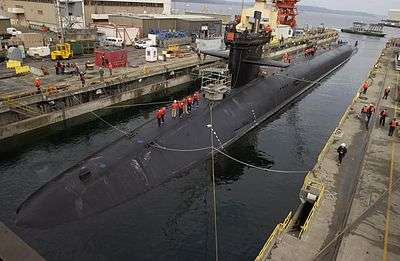 Submerged submarine moored in pier. Atop it are several people.