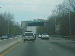 A four-lane freeway in an urbanized area. An overhead sign in the distance reads To George Washington Bridge with a blank variable message sign below it.