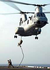 Marines descending from a helicopter with no equipment other than a rope