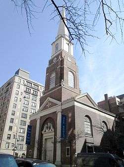 A brick church steeple with pointed wooden upper stage seen from below.