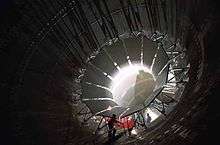 Photograph of workers working on large vanes arranged around the inside perimeter of the Unitary Plan Wind Tunnel.