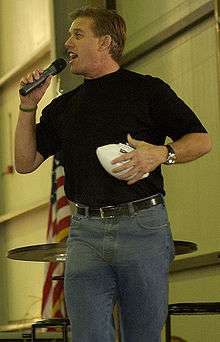 A man wearing a black shirt with blue jeans while clutching a football.