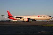 A Boeing 777-300ER in red and white livery with the Southern Cross painted on the tail. It is being parked on a sunny, cloudless day, facing right.