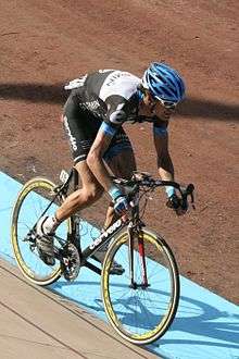 A road racing cyclist wearing a black and white jersey with blue trim and a conspicuous accented e on the shoulder, a blue helmet, and sunglasses.