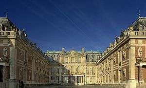 A courtyard with two wings of the ornate, two-story brick-and-stone palace coming from the right and left with the third side of the palace in the center.