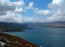 Colour photograph of a body of water surrounded by hills viewed from a hill