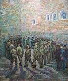 In an indoor prison yard a large group of men walk in a circle, one behind the other. The face of the prisoner in the centre of the painting and looking toward the viewer looks like Van Gogh.