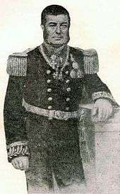 Engraved, three-quarters length portrait of a man with dark hair and sideburns leaning against a plinth and dressed in an elaborately embroidered naval uniform with a double-breasted tunic adorned with epaulettes and medals