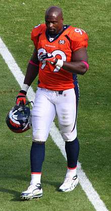 An American football player wearing an orange jersey with blue and white bottoms while walking.