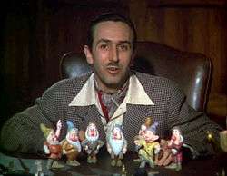 Walt Disney sits in front of a set of models of the seven dwarfs