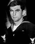 Head and shoulders of a young white man wearing a dark sailor suit with an eagle patch on the upper sleeve.