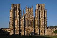 Yeloow stone building with buttressed towers on the left and right. Extensive decoration with statues.