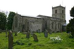 A long stone church in a graveyard, see from the northeast, with a north vestry, and a tower at the far end