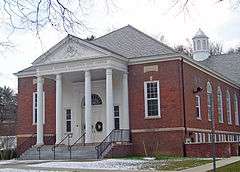 A brick building whose front section has a white triangular roof supported by columns. The inscription on the front reads "Bendheim West Greenwich Civic Center".