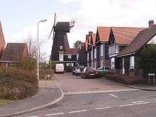 A view down a short cul-de-sac lined with houses, with a black windmill at the far end, facing to the left of the picture