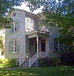 A tan-colored house seen through some branches and leaves in front of it