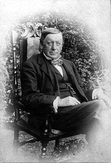 seated portrait photo of a dark-haired clean-shaven man aged 69