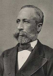 Head and shoulders photograph of a man in a Victorian suit.  He has a beard, a large mustache and is slightly balding.  He wears a serious expression and is looking slightly to the right.