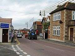 Street scene with houses and shops on both side of road on which there is a tractor.