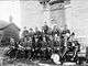 Black and white photograph of band members in uniform on front steps of stone township hall in 1894