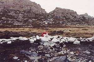 A cross amongst rocks painted white and a mountain in the background