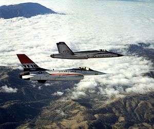 Two jet aircraft flying together over mountain range and cloud.