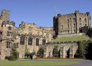 A courtyard in the foreground precedes a large medieval-style castle with a clock atop one of its peaks.