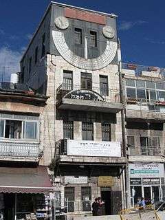 A narrow, four-story-high building with a large sundial on the fourth floor