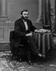 Photographic portrait of Grant sitting by a table with open book and top hat on it